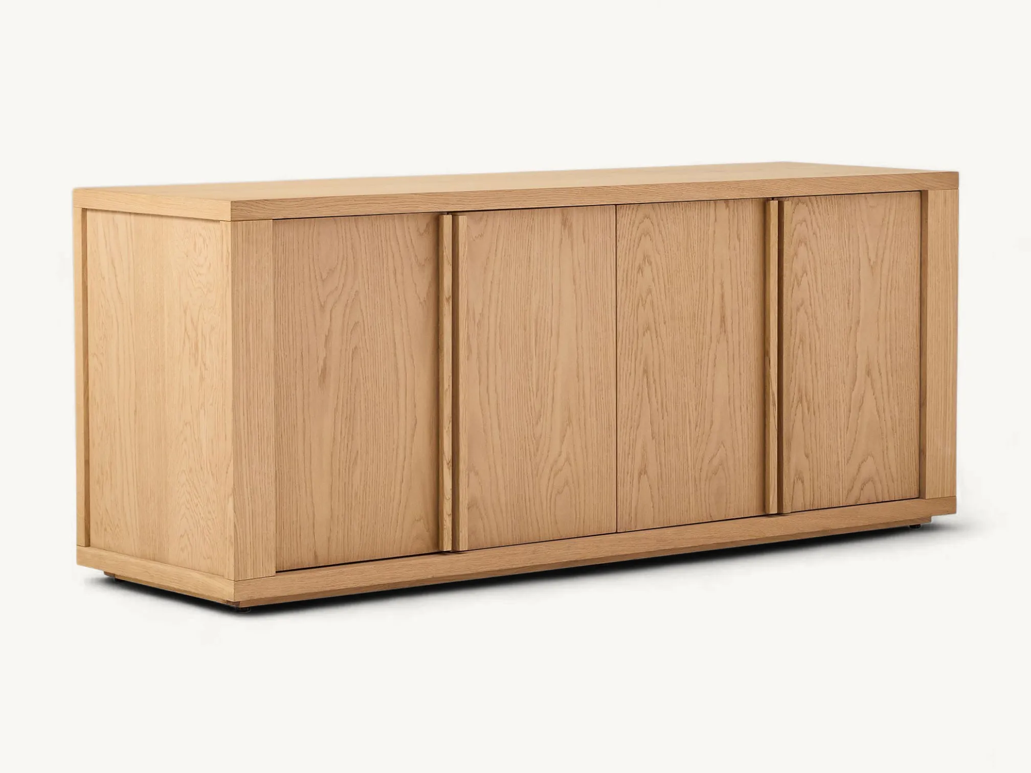Minimalist light oak-colored teak wood sideboard with four doors, vertical wood handles, and a low-profile plinth base in a bright interior setting.