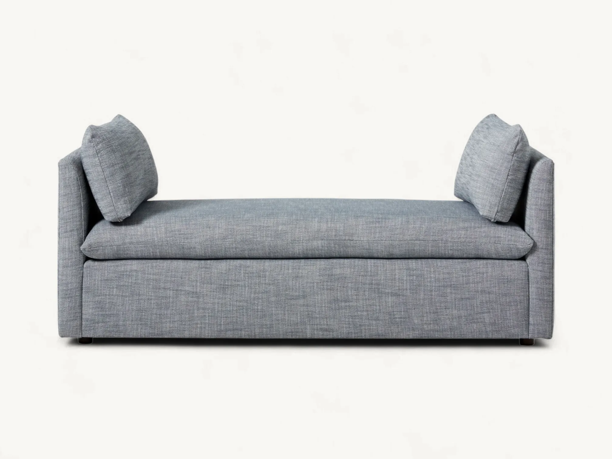 Modern upholstered bench in grey fabric with low side armrests and two rectangular accent pillows.
