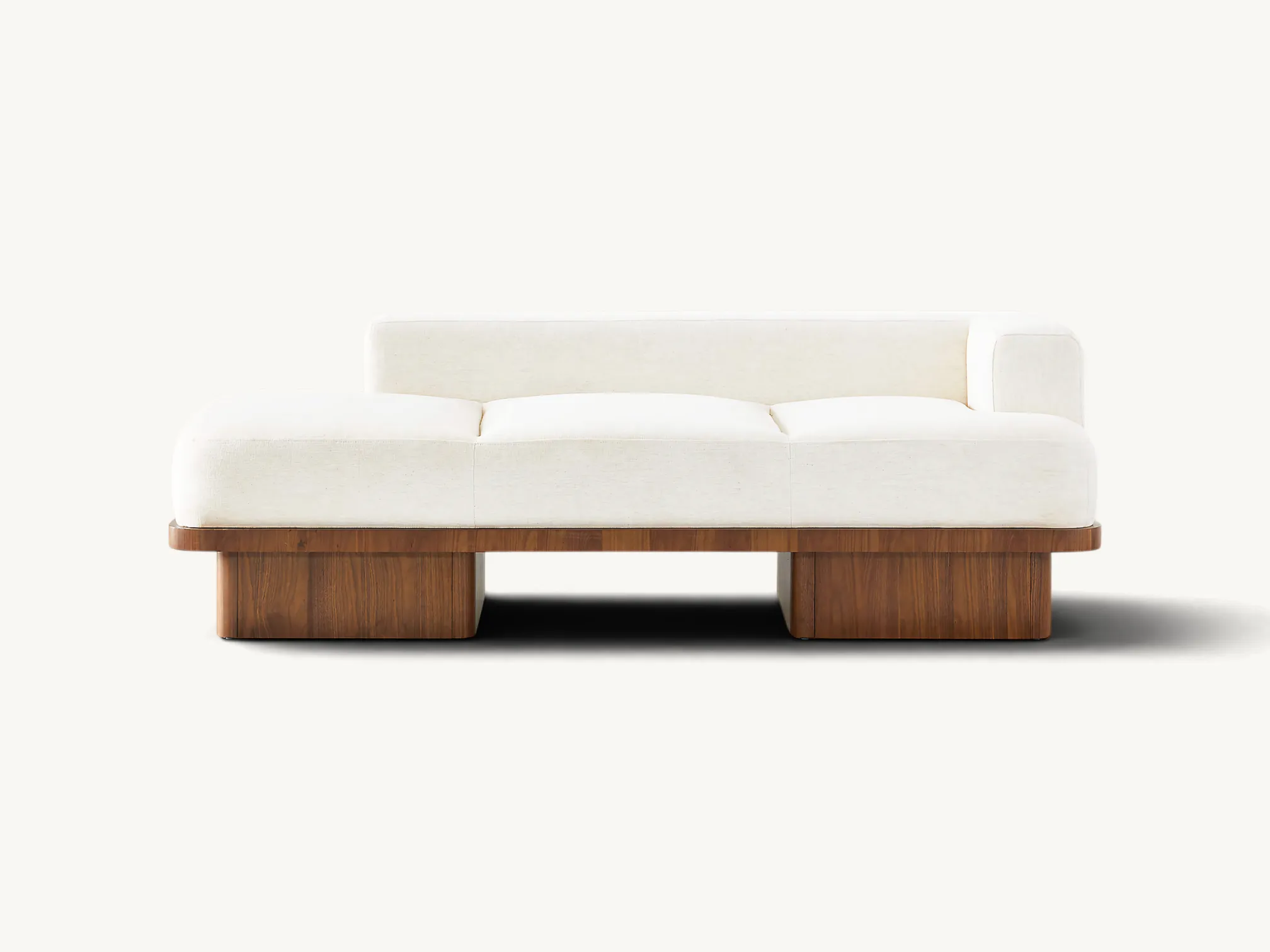 Asymmetrical cream fabric sofa with a thick solid teak wood base and rounded architectural legs.