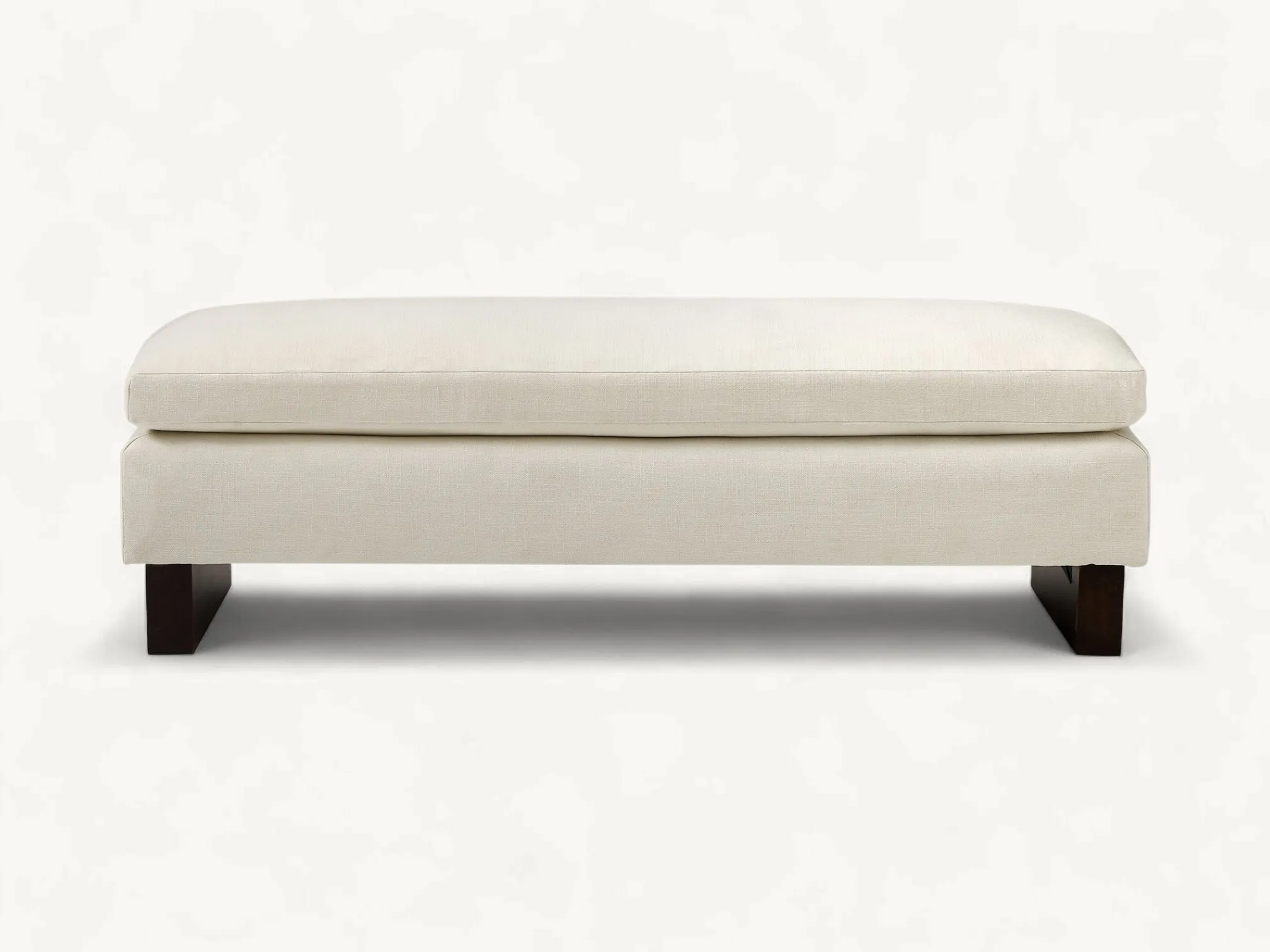 Sleek upholstered bench in off-white fabric with thick dark-brown teak wood block legs, styled in a bright minimalist bedroom.