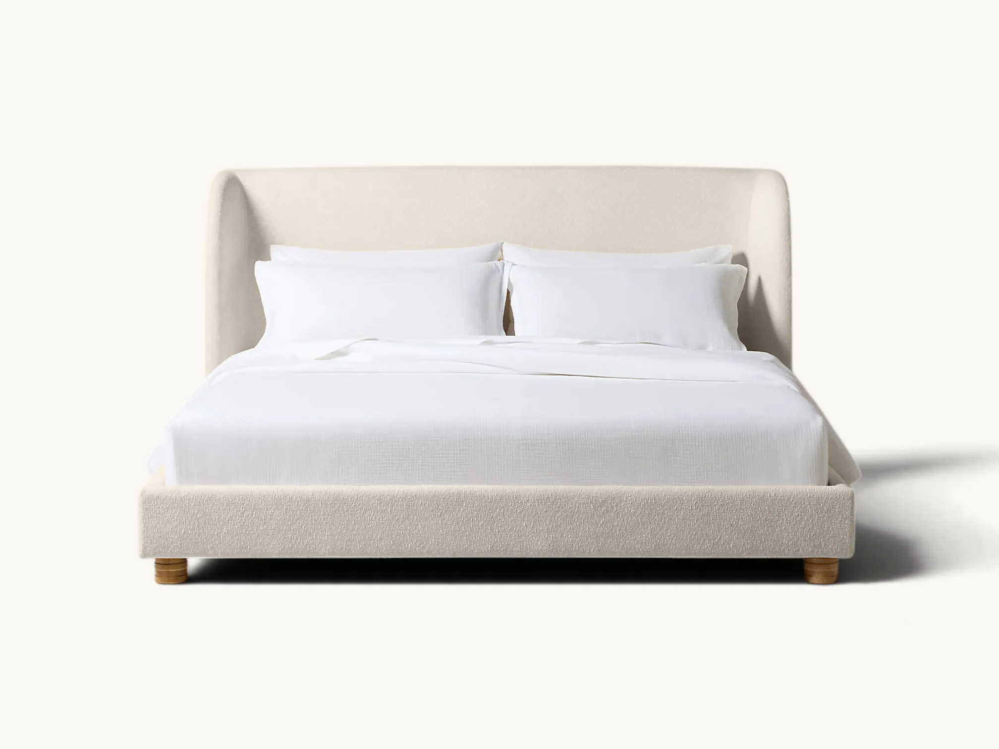Upholstered bed frame with curved wingback headboard and subtle wooden legs in a styled bedroom setting