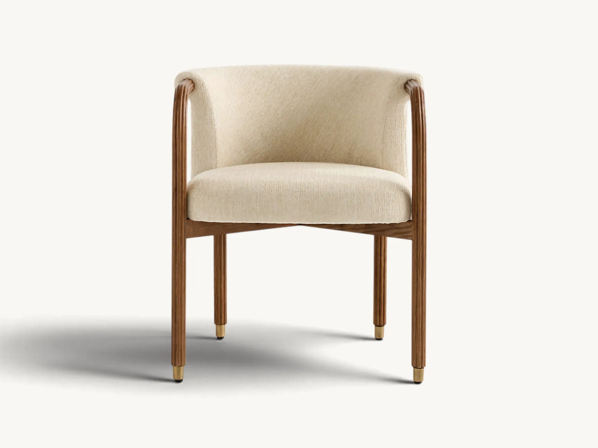 Upholstered dining armchair with curved beige fabric barrel backrest, fluted dark wooden legs, and brass-tipped feet